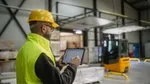 Factory workman wearing protective florescent uniform working on an iPad in a manufacturing warehouse.