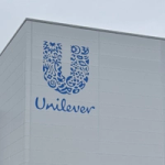 Unilever logo on the exterior wall of a factory building against a cloudy sky.