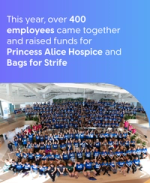Large group of employees in matching blue shirts gather in an atrium to celebrate fundraising for two charities.